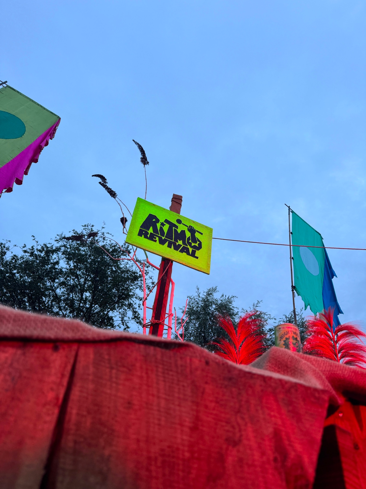 Neon green Ritmo Revival sign against a dusk sky at a festival